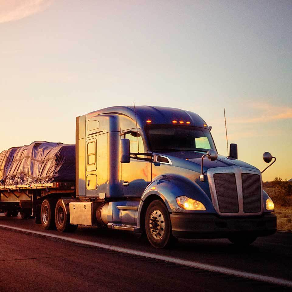 Cropped view of flatbed shipping truck driving at sunset