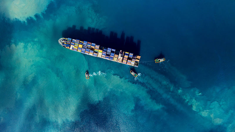 Luftaufnahme eines Containerschiffs, das aufs Meer hinaus geführt wird