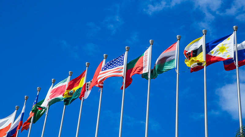 several country flags flying in a row against a blue sky