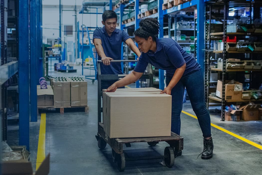 Two warehouse workers loading a box onto a dolly cart