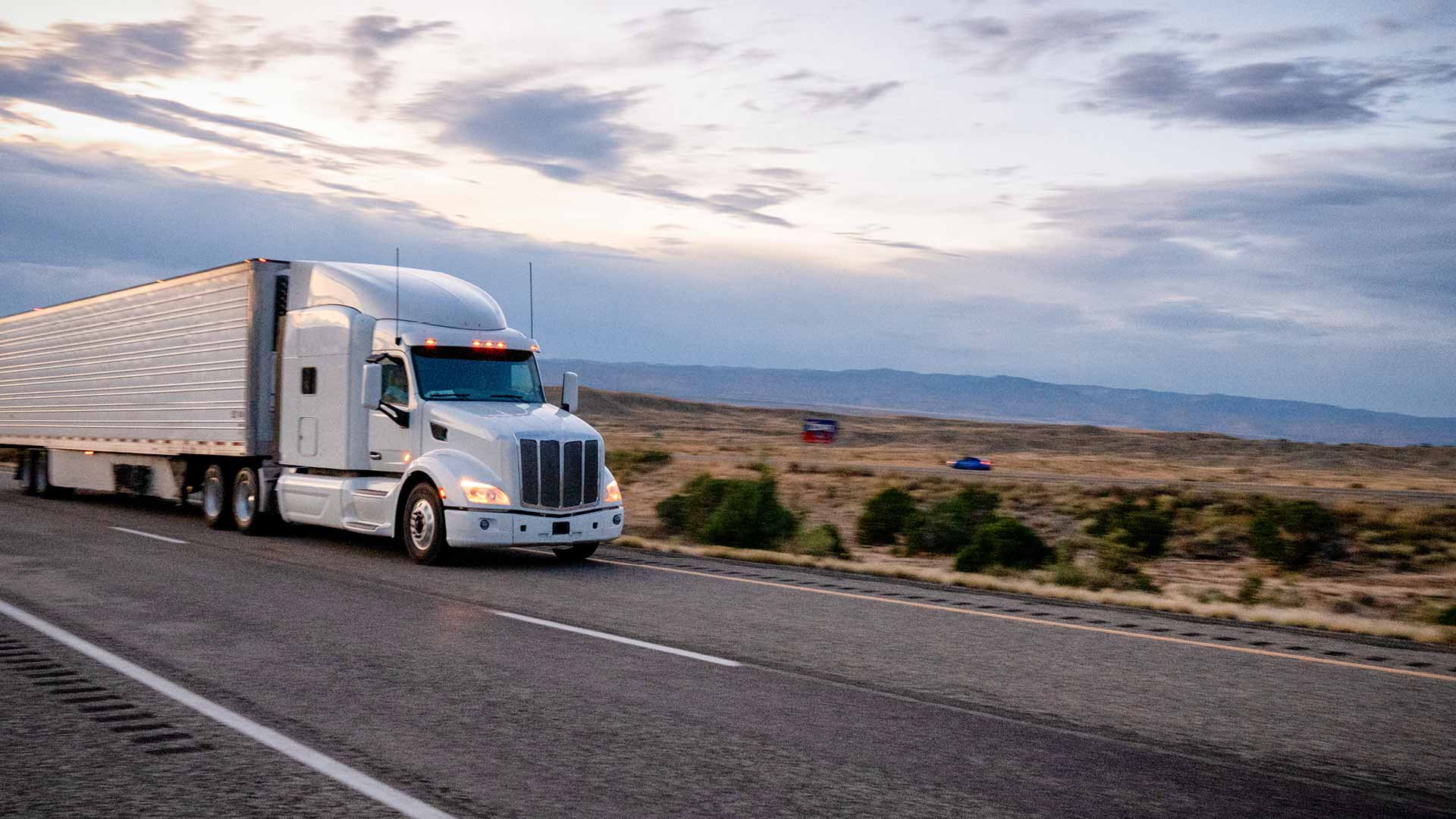 Cropped white semi-truck driving on a two lane highway at sunrise