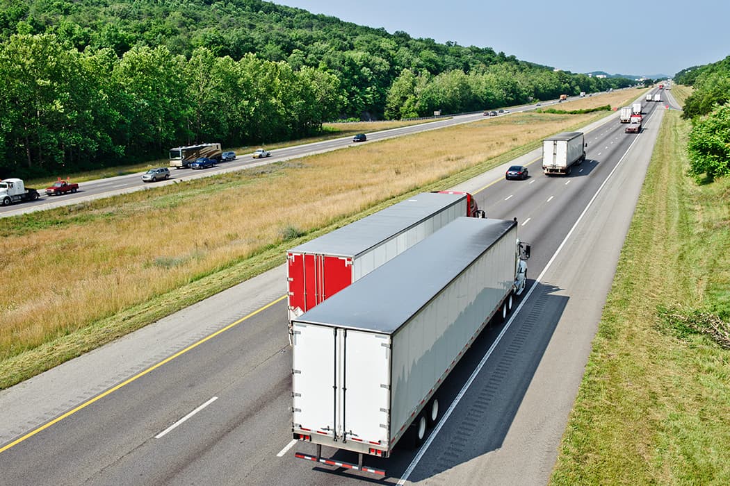 Rear-aerial view of full truckloads on an open freeway in Spring